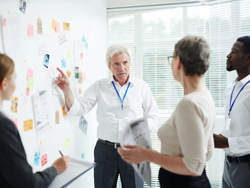 Project manager staat tegenover groep mensen bij een whiteboard om problemen te bespreken