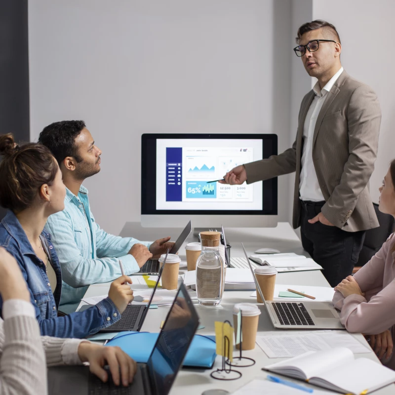 Consultant in de sector IT en Technologie, wijzend naar scherm met daarbij 4 andere aanwezigen die naar hem luisteren