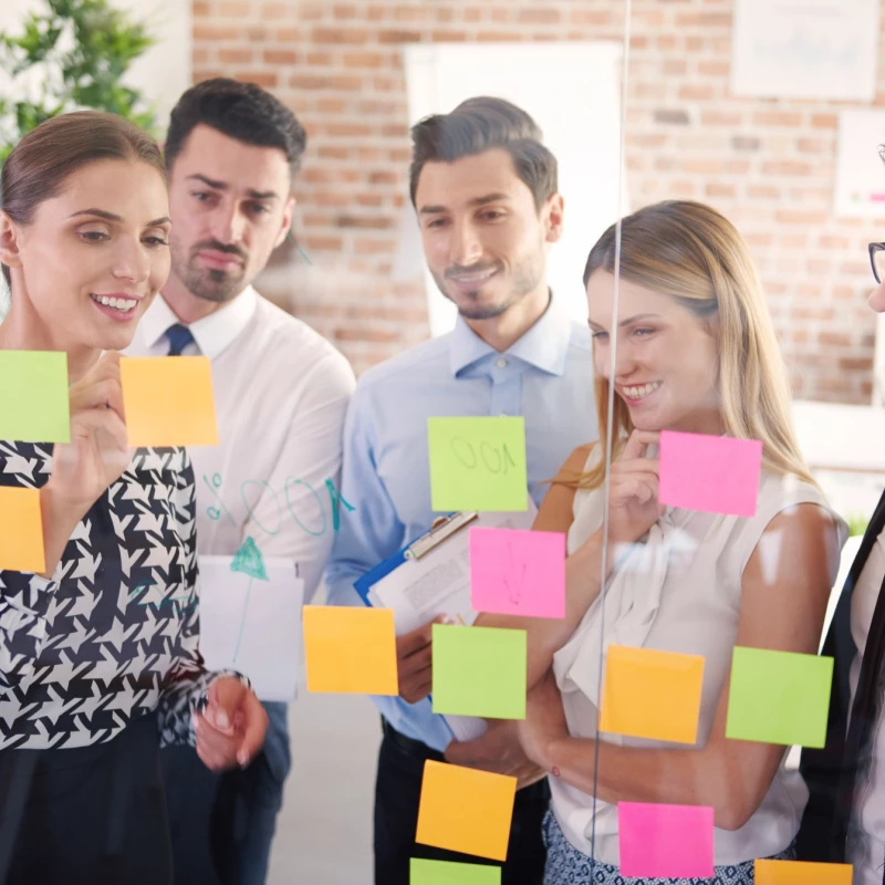 Groep mensen die tijdens een Lean Six Sigma workshop aandachtig naar de post-its kijken en deze interactieve aanpak sterk waarderen