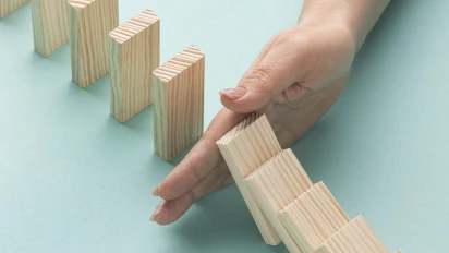 Houten domino blokjes die omvallen met een hand ertussen die dat stopt, vergelijkbaar met risico beperking met FMEA